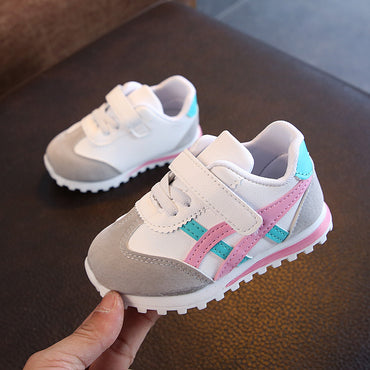 Children's sneakers with gray, pink, and blue design held by a hand on a dark surface.